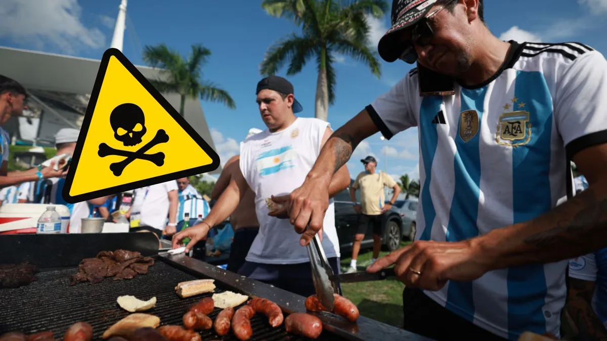Two men working on a large grill with palm trees in the background and a skull and cross bones warning label