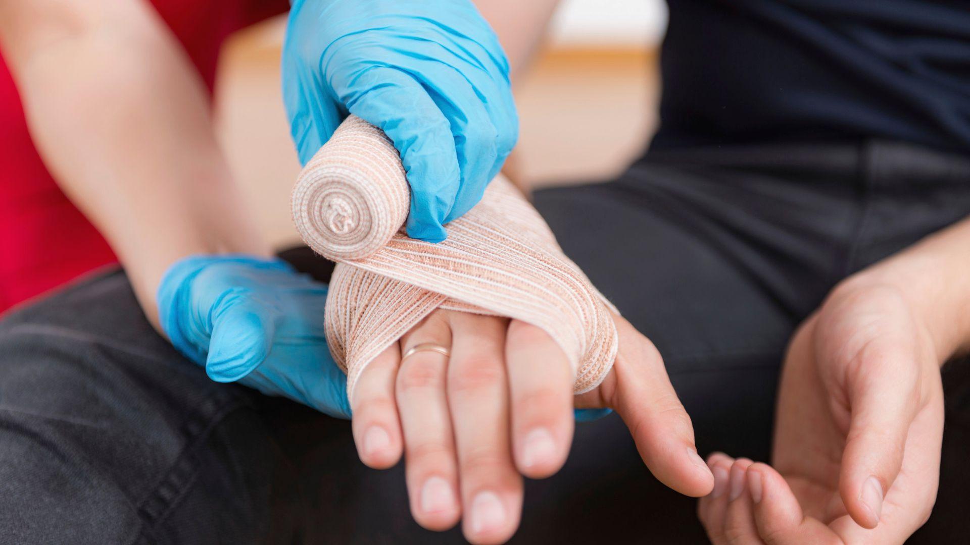 Illustrative stock photograph of a gloved person bandaging a hand.