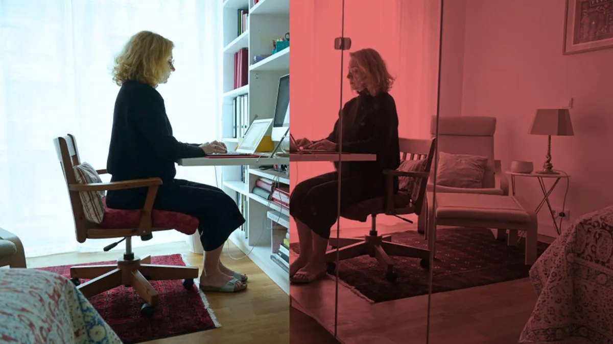 A woman works from home on her laptop in her bedroom in front of a mirror that displays her reflection