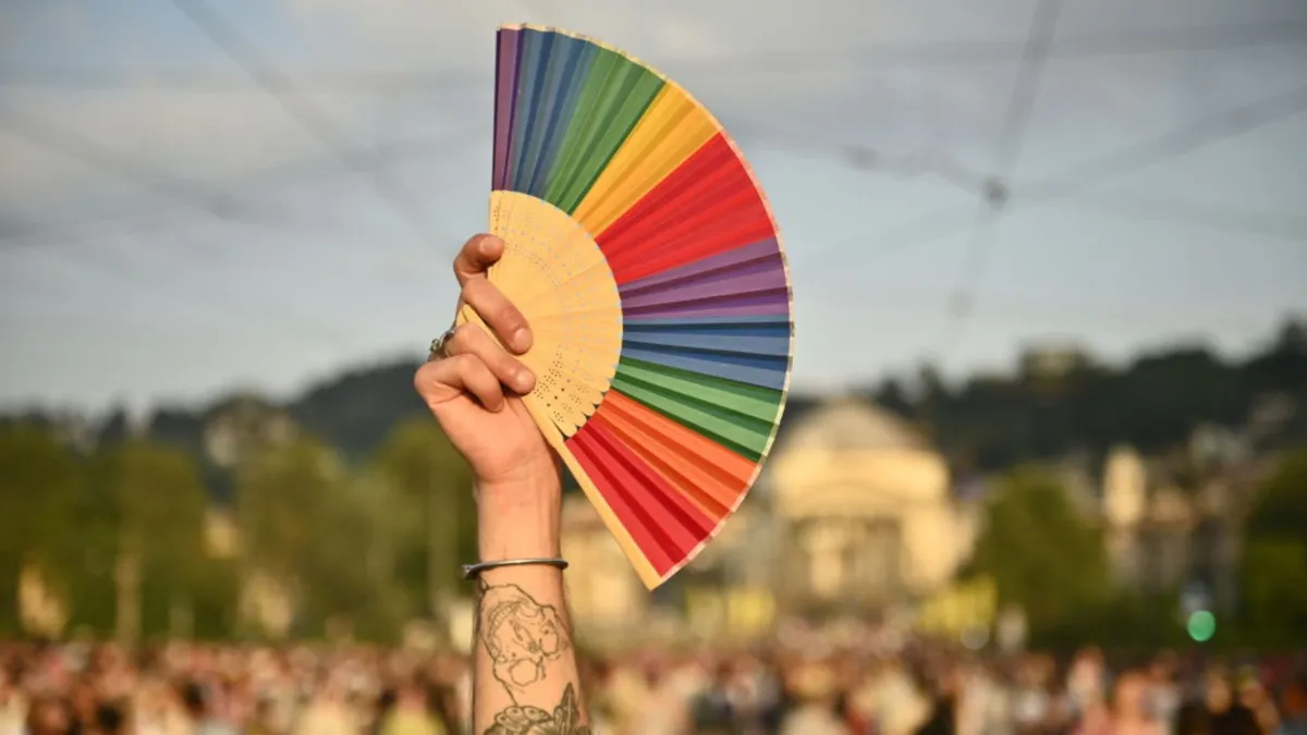 A person holds a rainbow colored fan at a large parade
