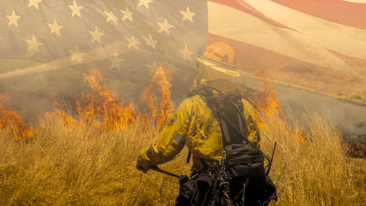 A firefighter stands in front a field on fire with an American flag overlaid on the photo