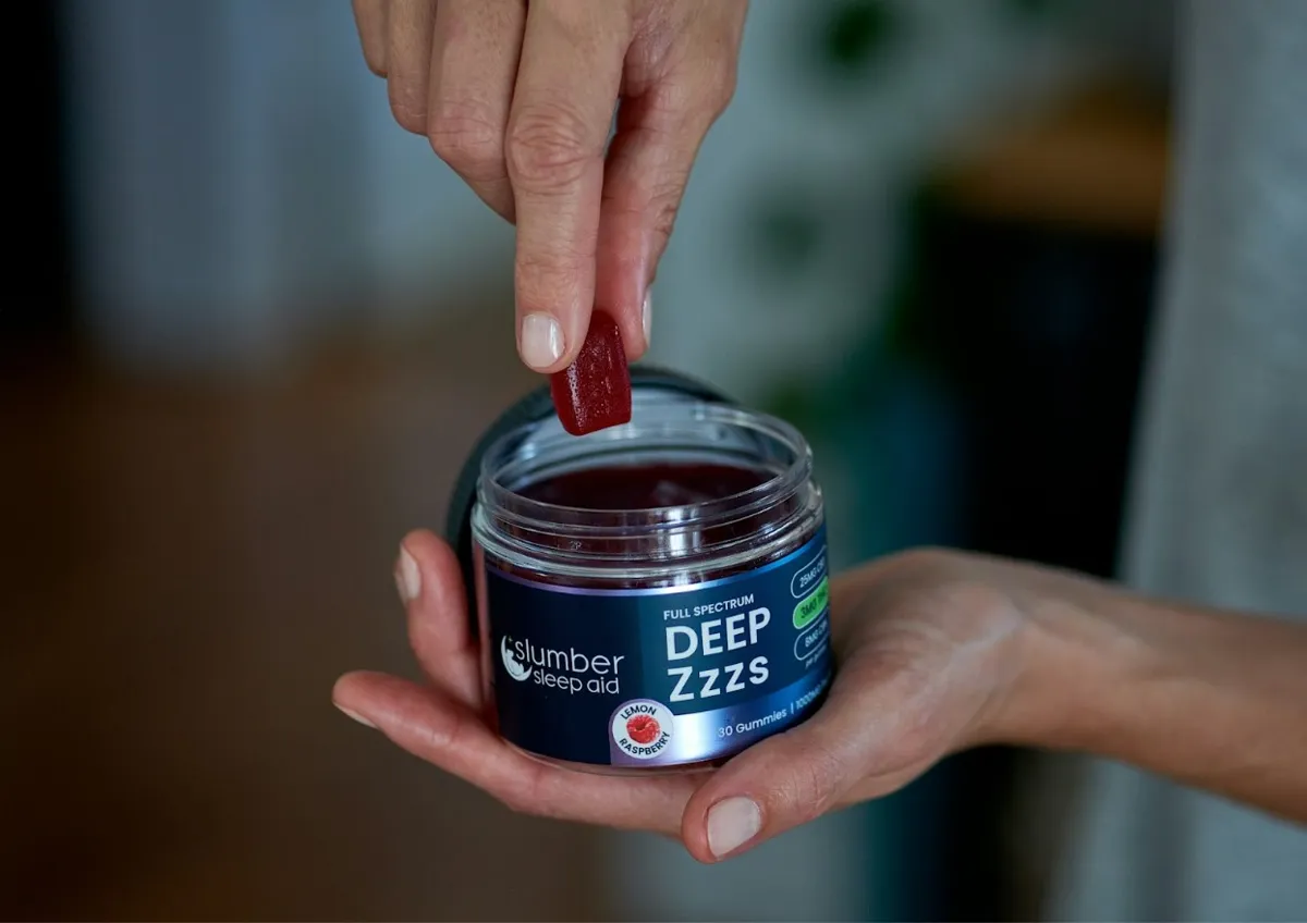 A person holding a gummy sleep aid from a blue jar
