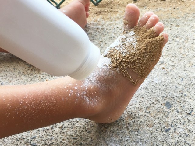 Loose powder being applied to a sandy foot.