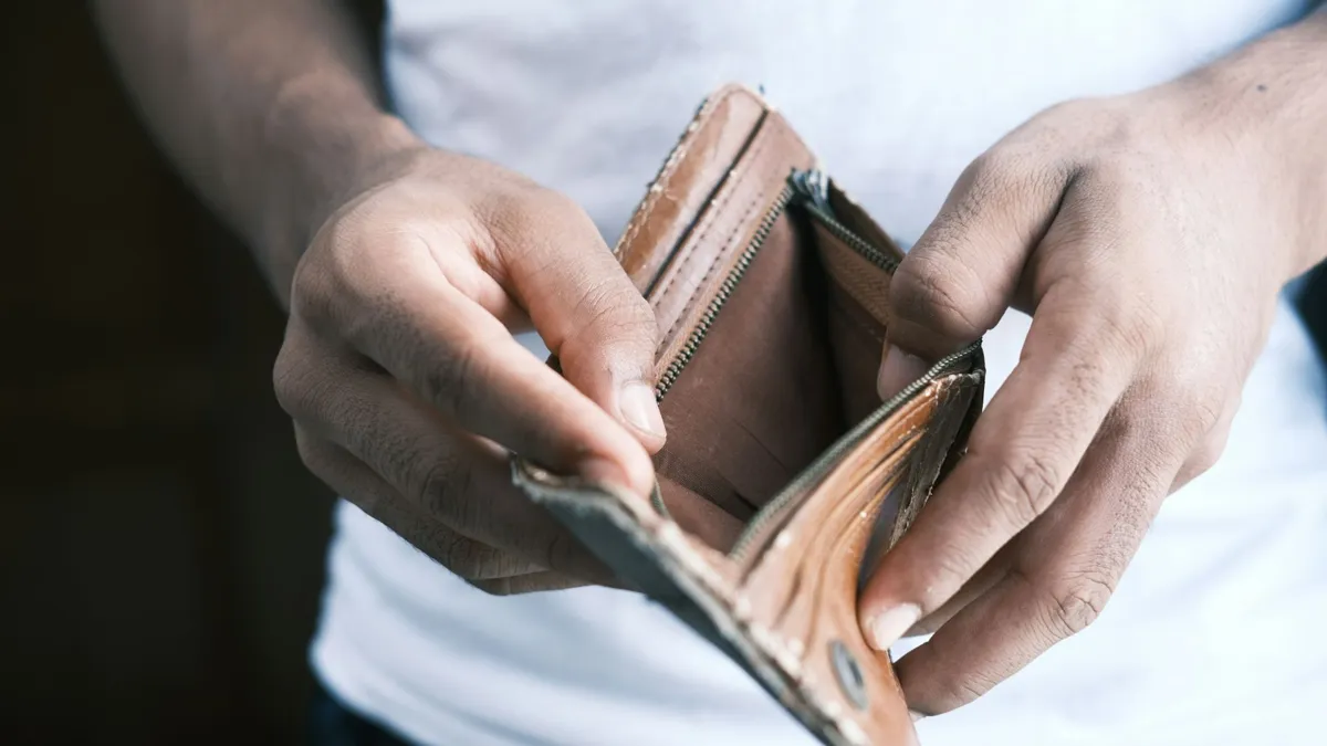 A man holds open an empty leather wallet