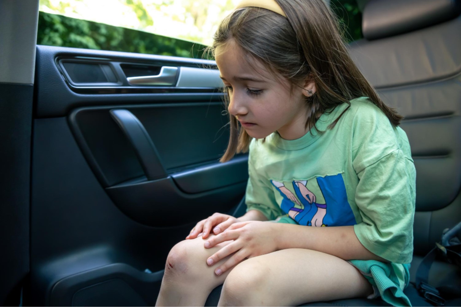 Child sitting in a car’s rear seat with no restraint visible.