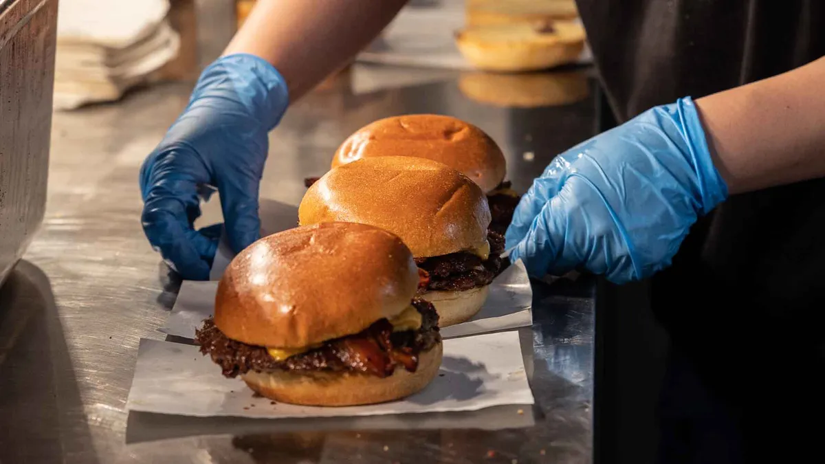 A fast food employee prepares some bacon cheeseburgers