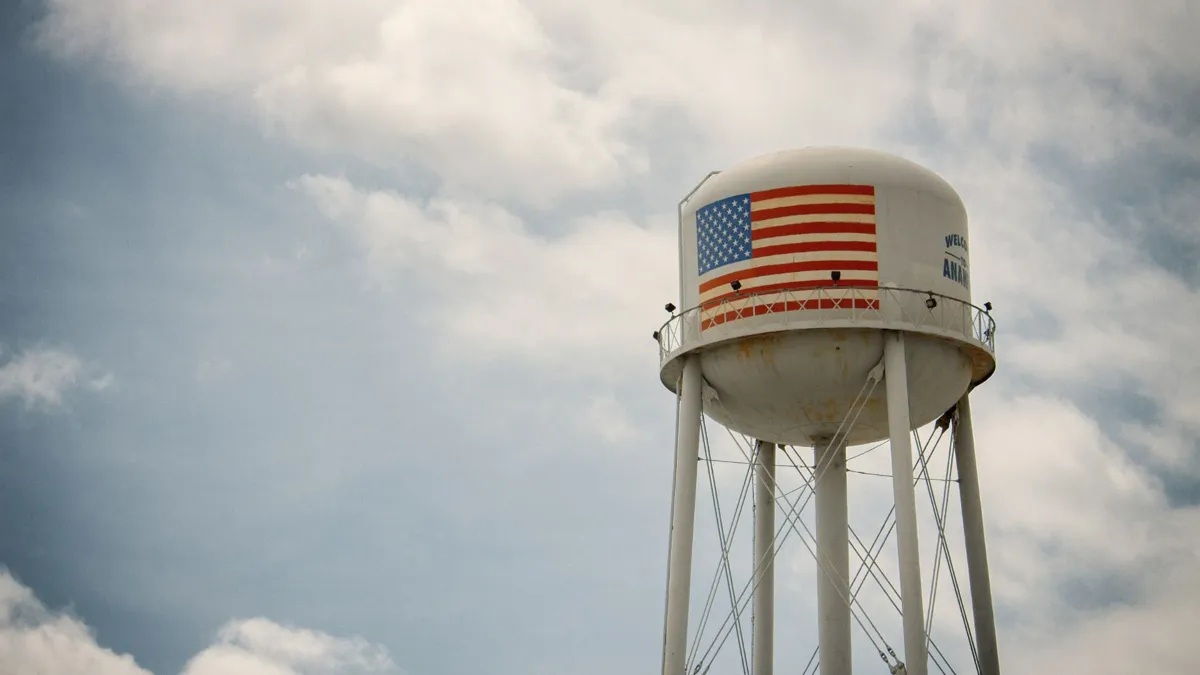 A large white water tower with an American flag set against a blue sky with clouds