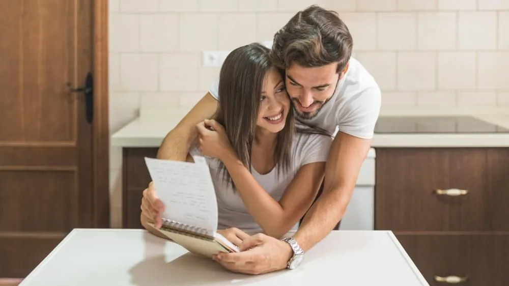 A couple smile as they reflect on the goals they have achieved while they sit in their kitchen