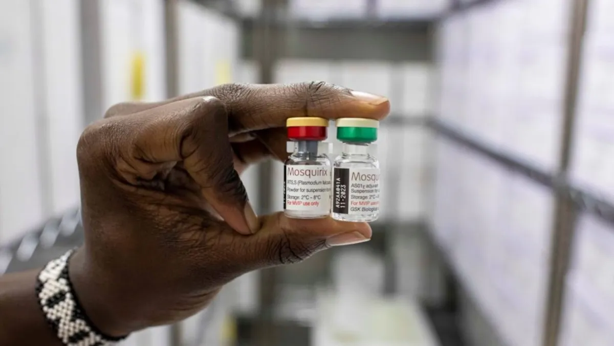 A person's hand is holding two vials of the RTS,S malaria vaccine labeled 'Mosquirix'. One vial has a red cap and the other a green cap