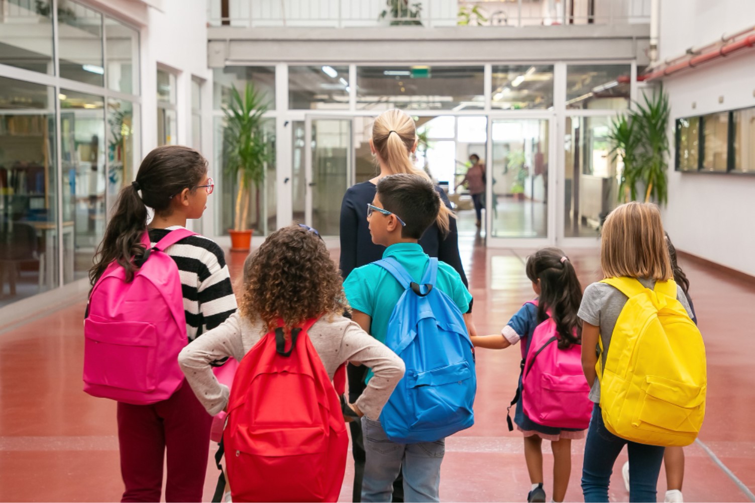 Children with backpacks and an adult inside a school building.