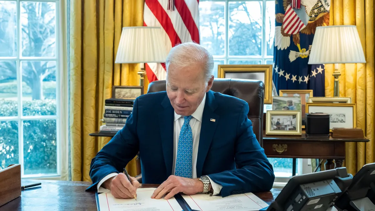 President Joe Biden signing papers in the Oval Office.