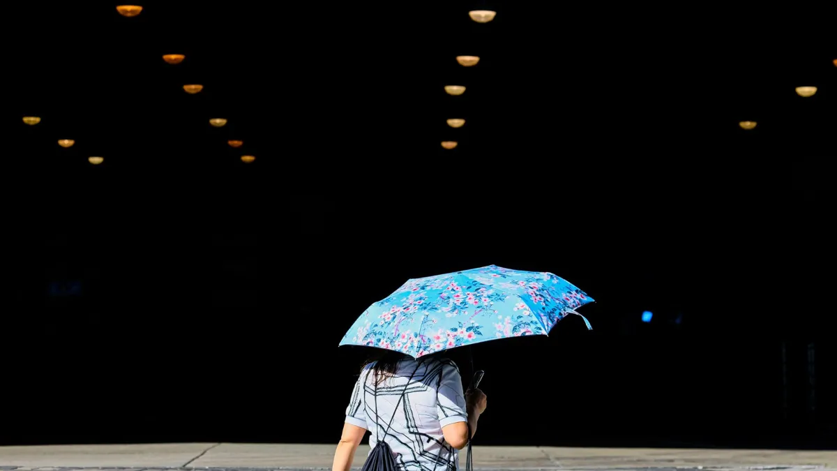 A woman walking underneath an umbrella outside because of the sun.