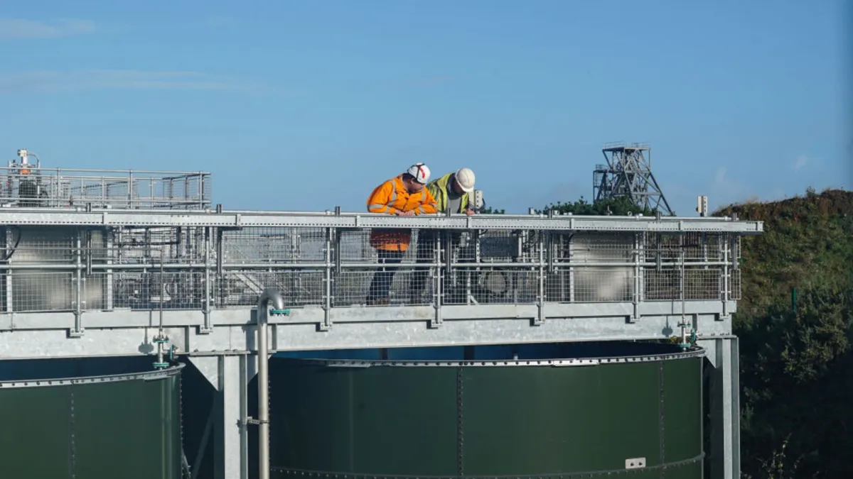 Two men wearing hard hats and PPE stand on the bridge of a water treatment plant