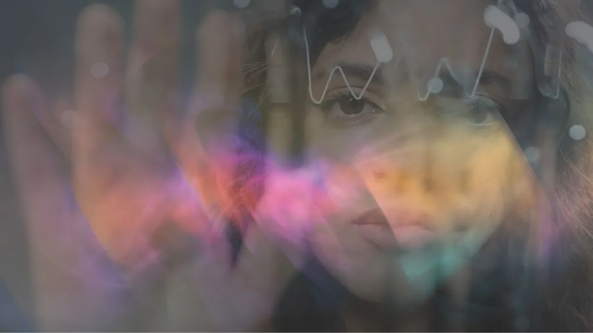 A person holds their hand to the camera as the see visual synesthesia waves, and is overlaid by rainbow colors.