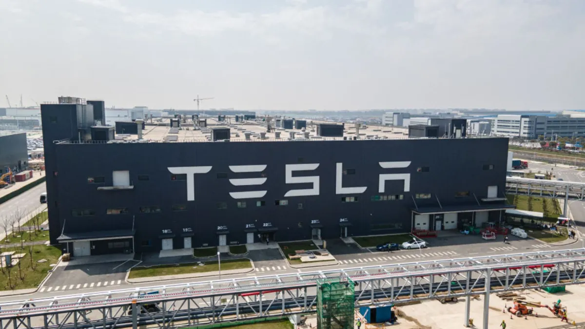 A large black factory with the word "TESLA" written in large white letters. A large road crosses in front of the factory