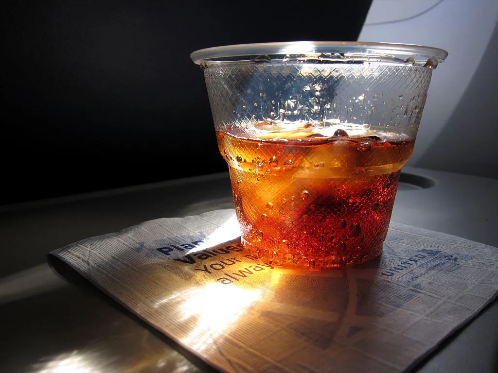 Rum and coke in sunlight on airplane tray table during flight