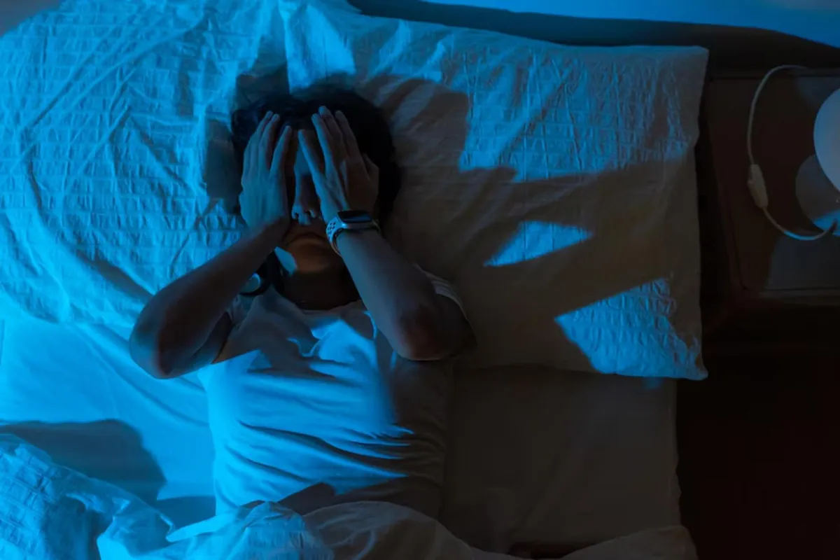 A person holds their head in their hands, struggling to sleep in bed