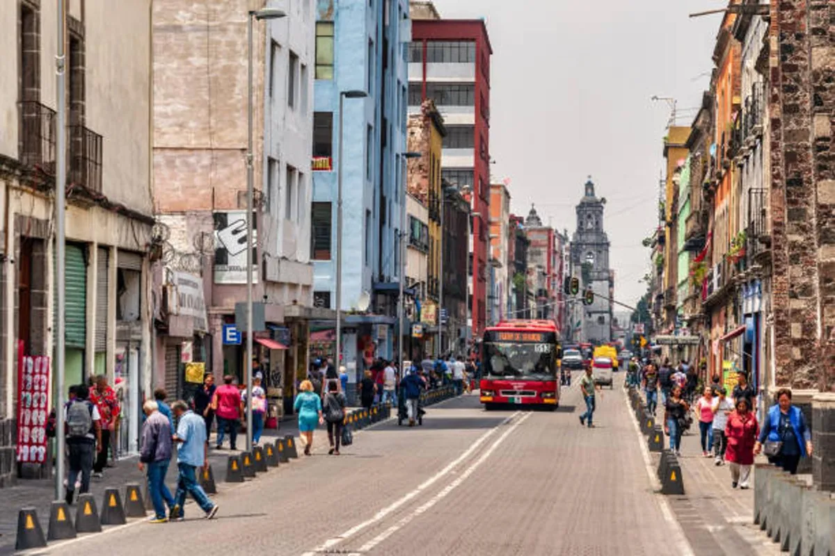 A photograph of a street with pedestrians and a large red bus in Mexico City