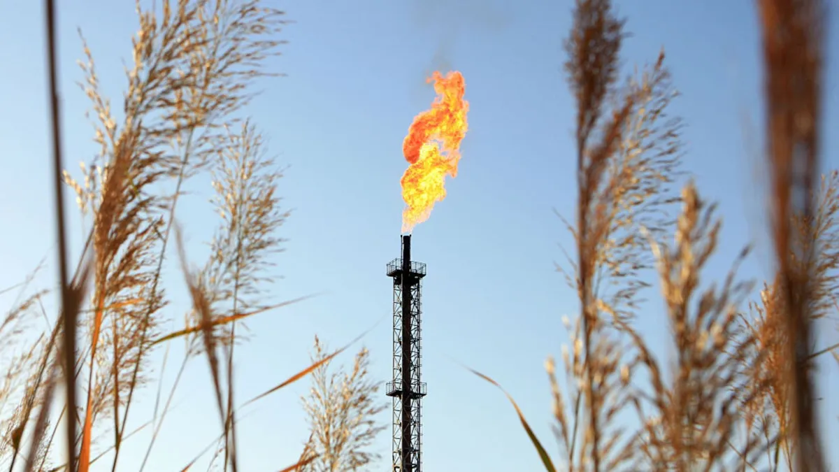 A large oil tower with a large plume of fire surrounded by wheat