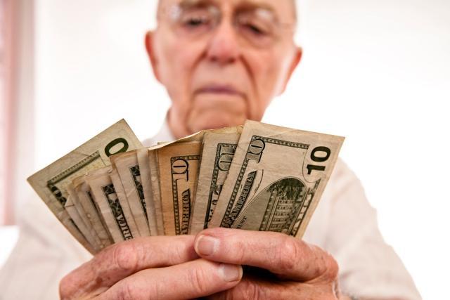 An older person holding cash; illustrative archive photograph, not a verified financial circumstance.