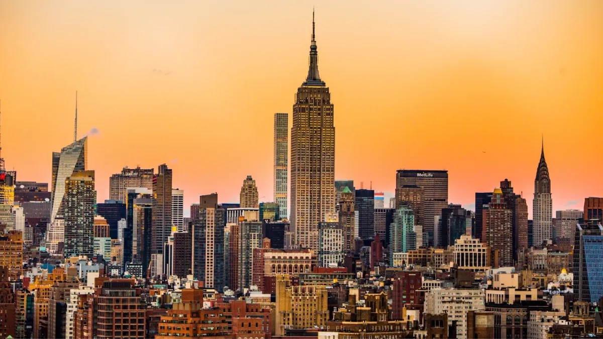 The New York City skyline at sunset, showcasing the iconic Empire State Building in the center with a backdrop of an orange sky