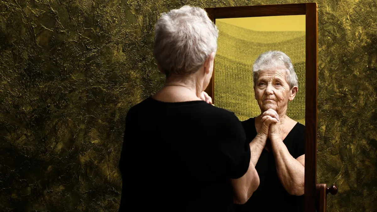 An elderly woman examines herself in a mirror