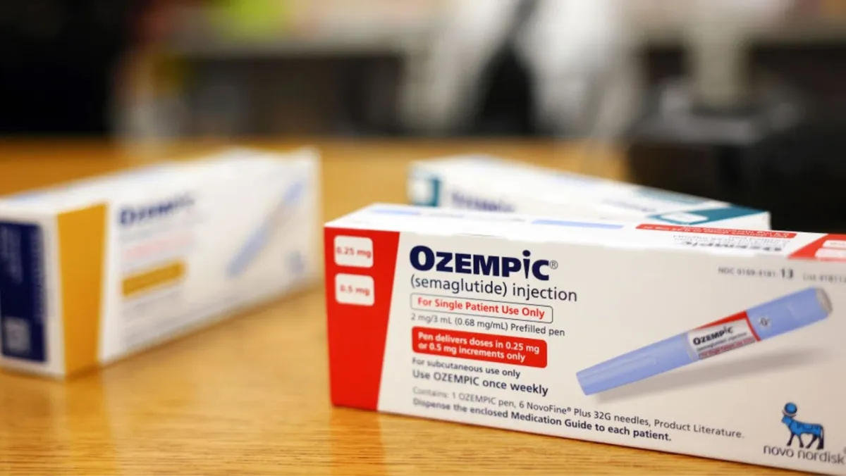 Two boxes of Ozempic (semaglutide) injection pens are positioned on a wooden table. The foreground shows a box labeled for 0.25 mg doses, and the background box is for 0.5 mg doses