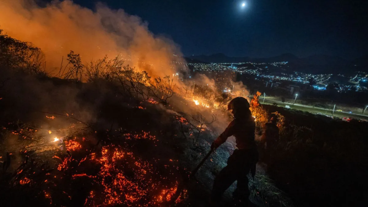 A firefighter works next to a blaze on a hill at night
