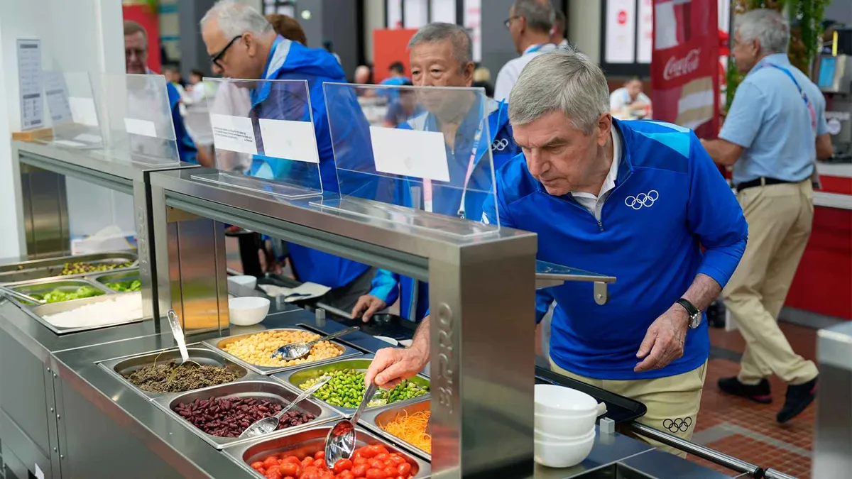 IOC President Thomas Bach tries food from a salad bar while touring the Olympic Village ahead of the start of the Paris 2024 Olympic Games on July 22, 2024 in Paris, France.
