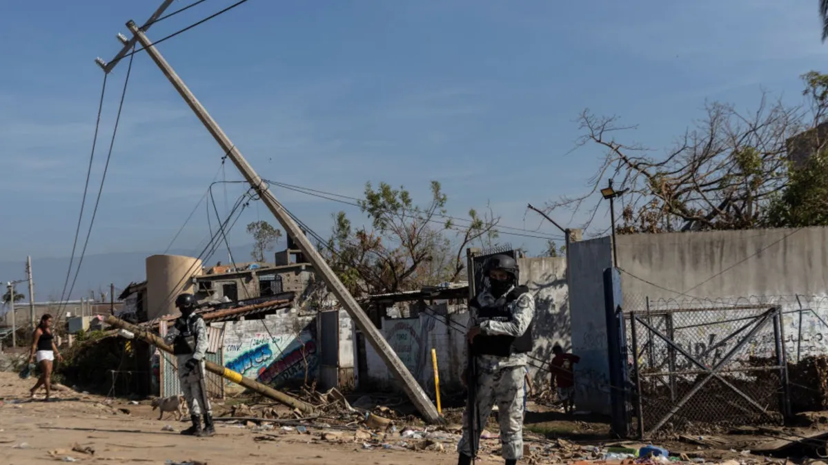 Armed guards stand in front on down power lines, destroyed infrastructure, and trees