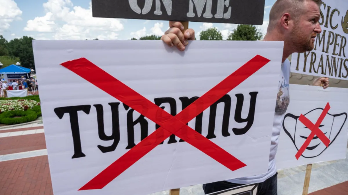 A man holds a sign with the word "Tyranny" crossed out with a large red X