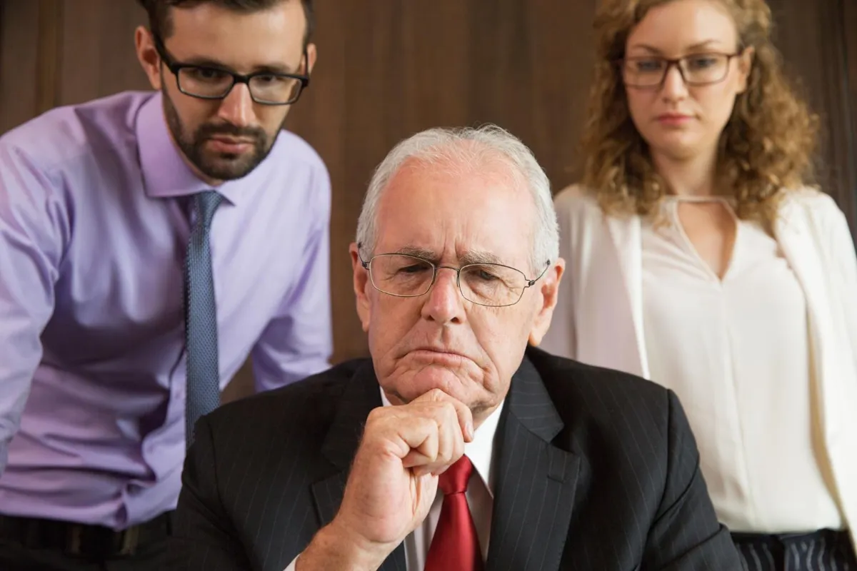 Two employees stare over the shoulder of an older worker at their company