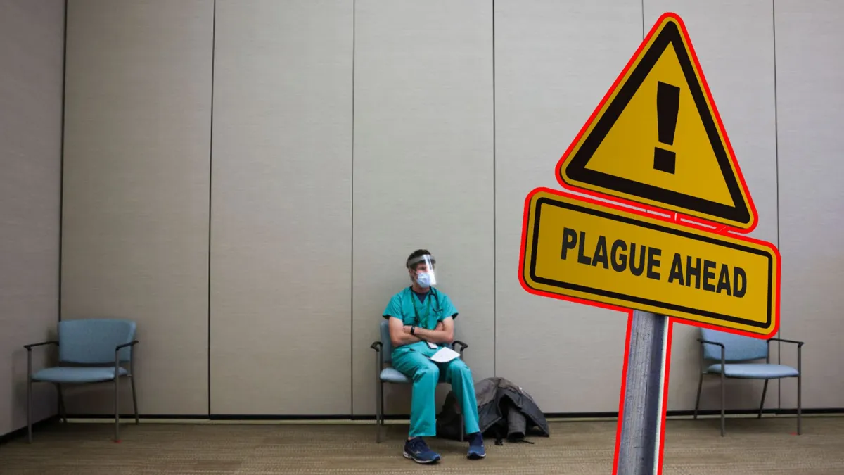 A doctor sits in a single chair in a hospital waiting room wearing a shield and a face mask with a warning sign that reads "plague ahead"
