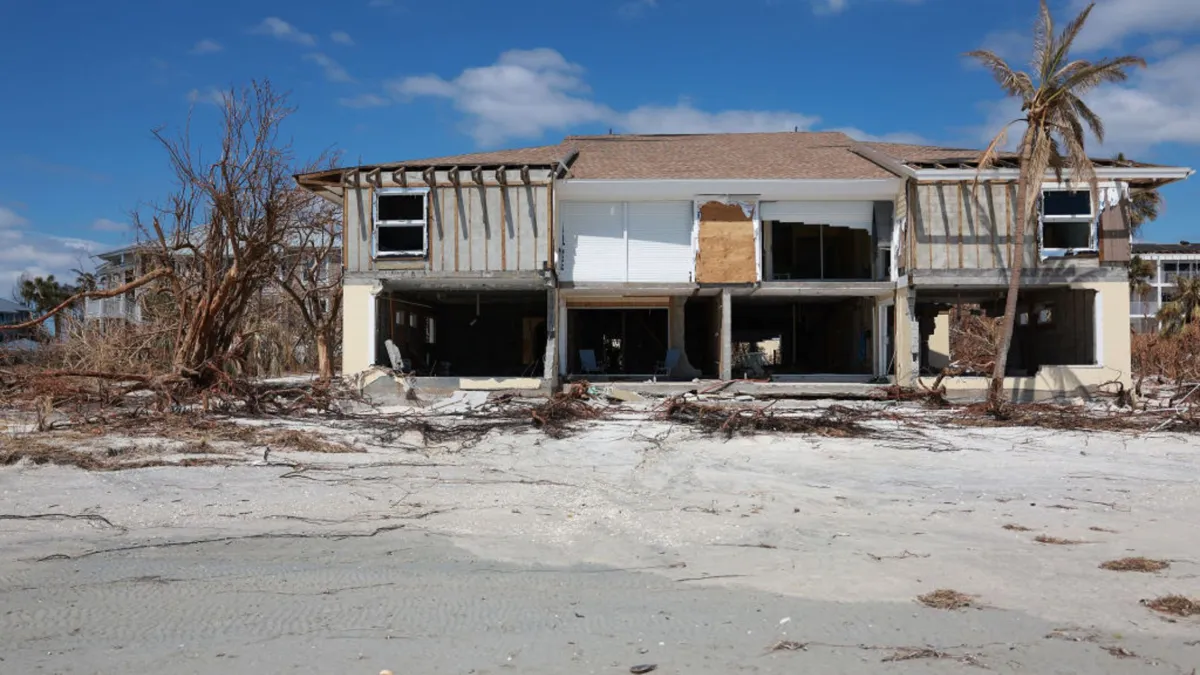 A large beachfront house destroyed next to downed tree limbs on a sandy beach