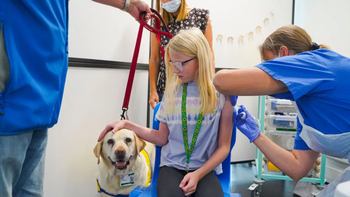 A young girl petting a dog while receiving a vaccination in her left arm