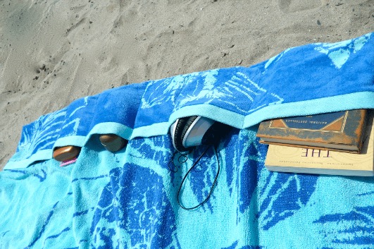 Blue beach towel with sewn pockets holding small items.