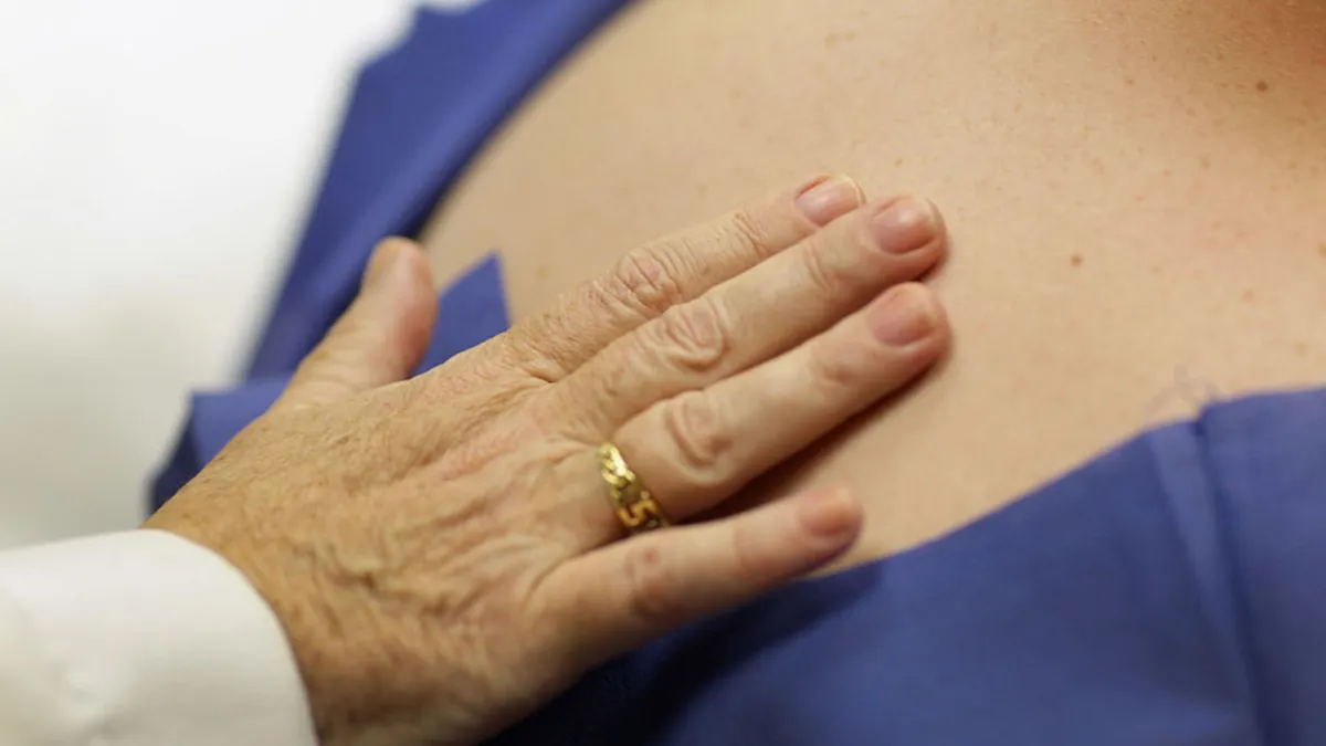 A person holds their hand with a gold wedding ring against the back of a patient wearing a blue smock