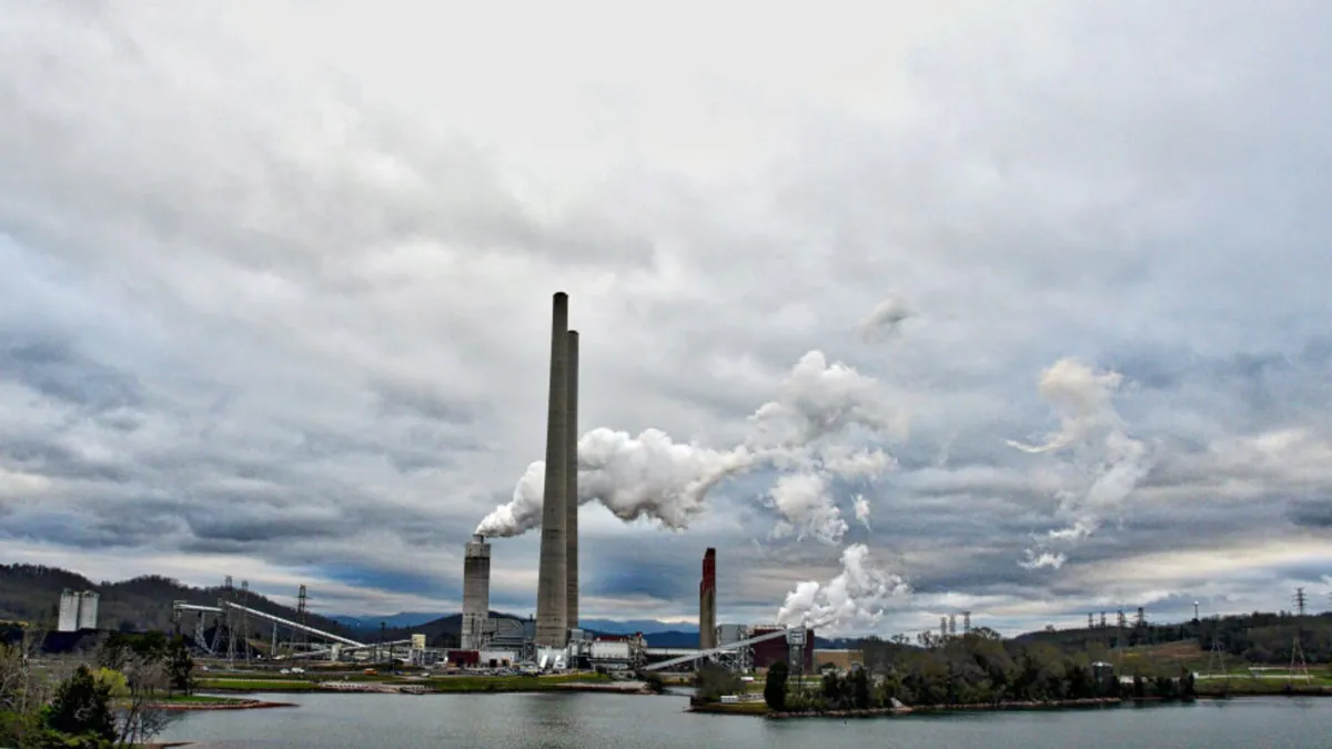A large coal plant next to a body of water emitting large plumes of smoke