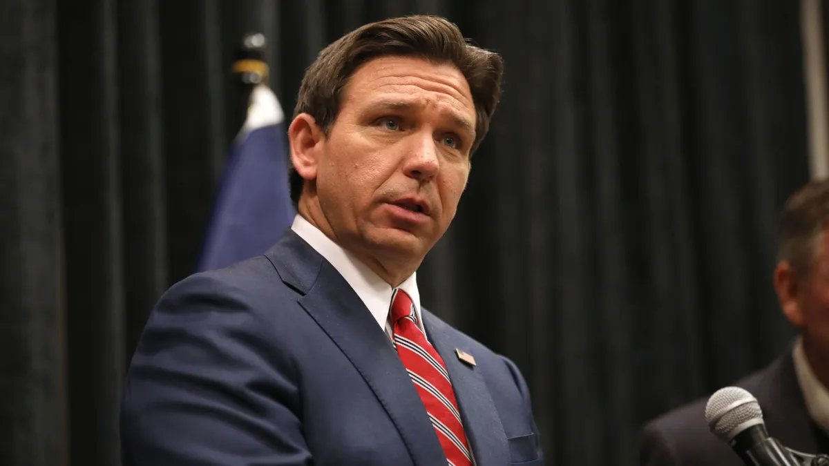 Ron DeSantis wearing a suit standing in front of a microphone.