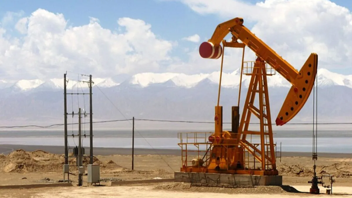 A small red oil drill working on dry land in front of a large mountain range