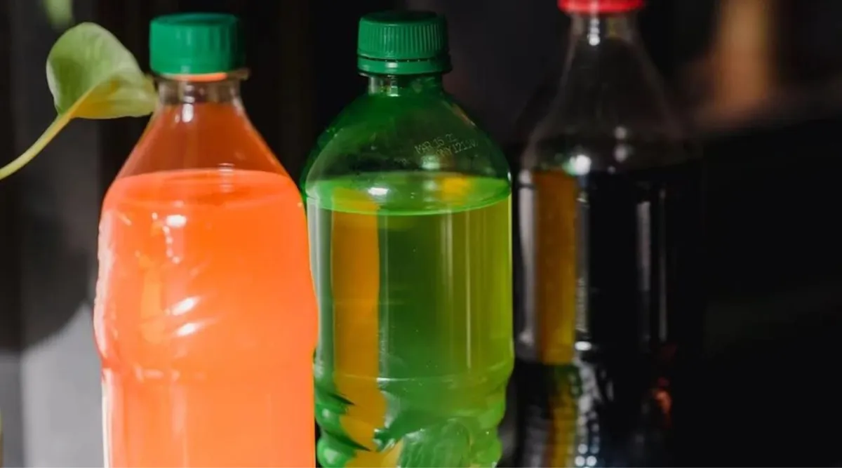 Three bottles of soda in a diagonal line. One bottle is orange, one is green, and the other is black. The orange and green bottles have green lids and the black bottle has a red lid.