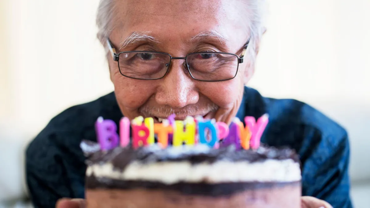An older man holds a cake with birthday candles