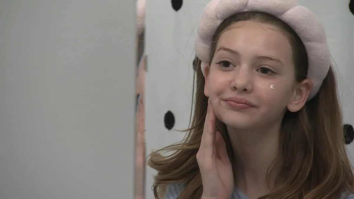 A young girl in a headband applying lotion to her face