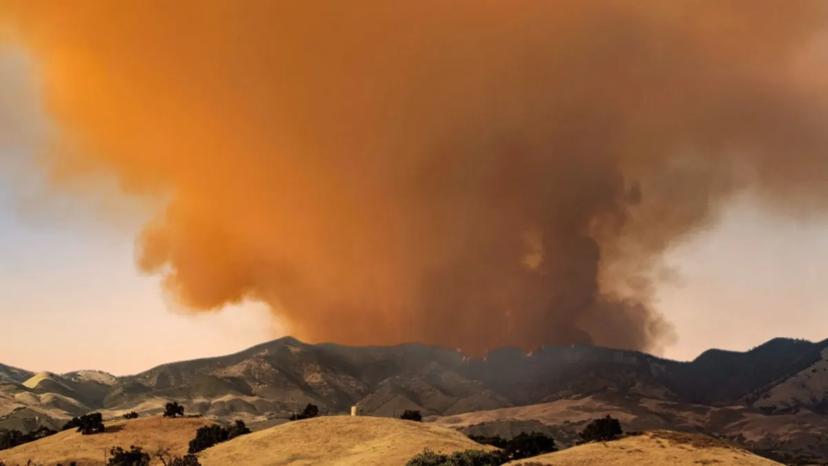 A large plume of smoke hovers above a dry mountain