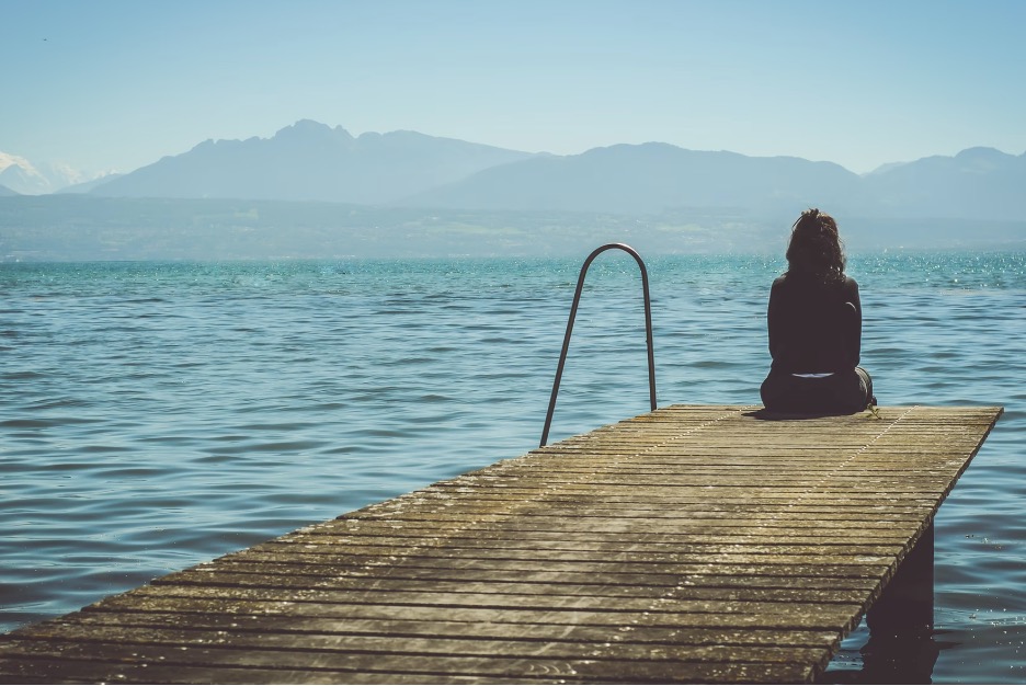 A person sitting alone on a wooden pier beside a lake