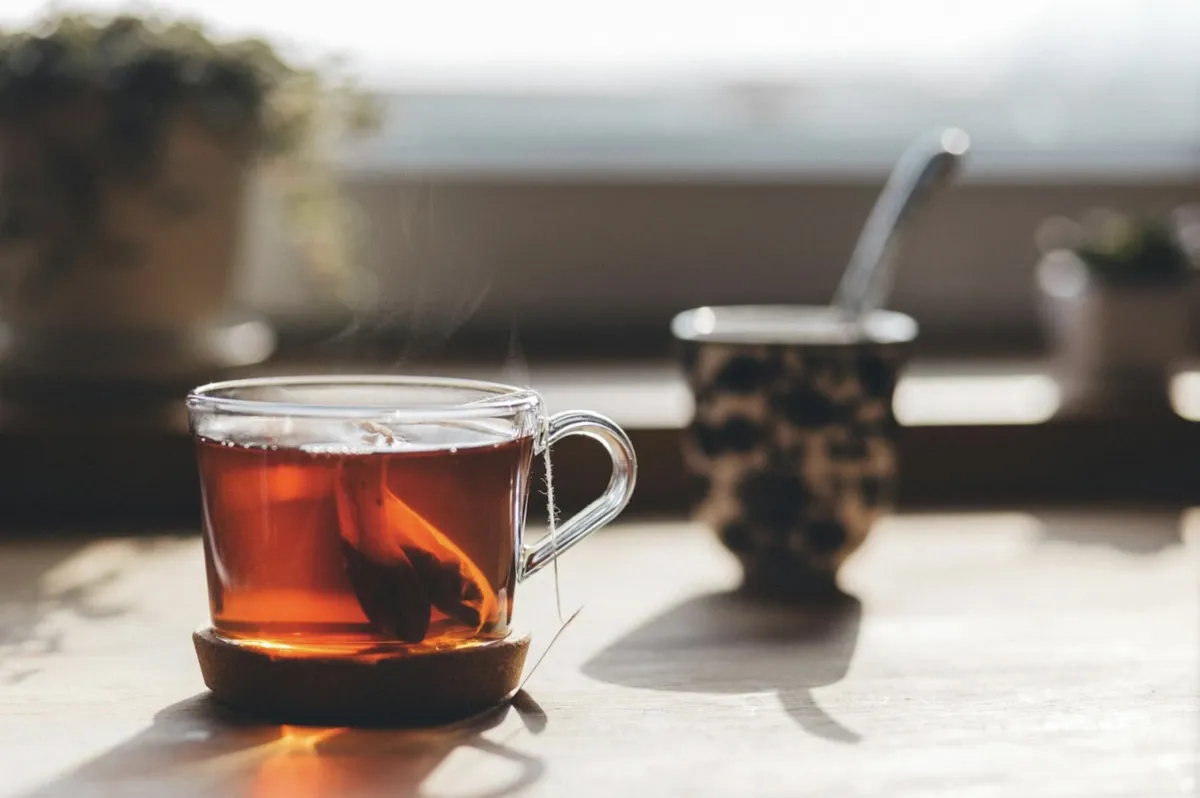 A teacup filled with tea and tea bag on a table under the sun