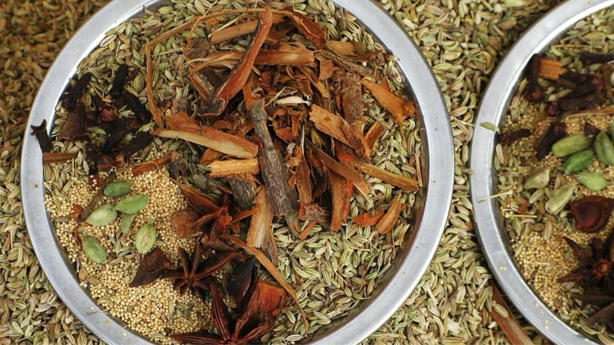 Two round metal bowls filled with a variety of whole spices. The spices include star anise, cinnamon sticks, green cardamom pods, fennel seeds, and coriander seeds