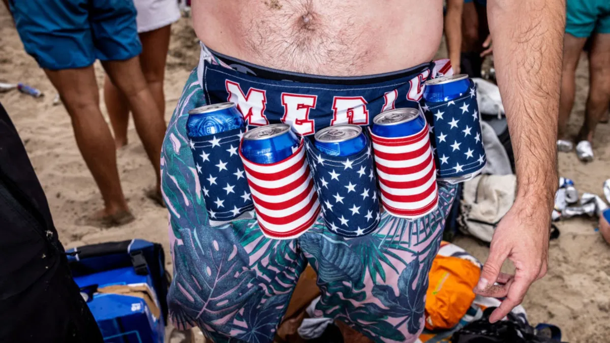 A man wearing swim trumps with 5 beers wrapped around his waist.
