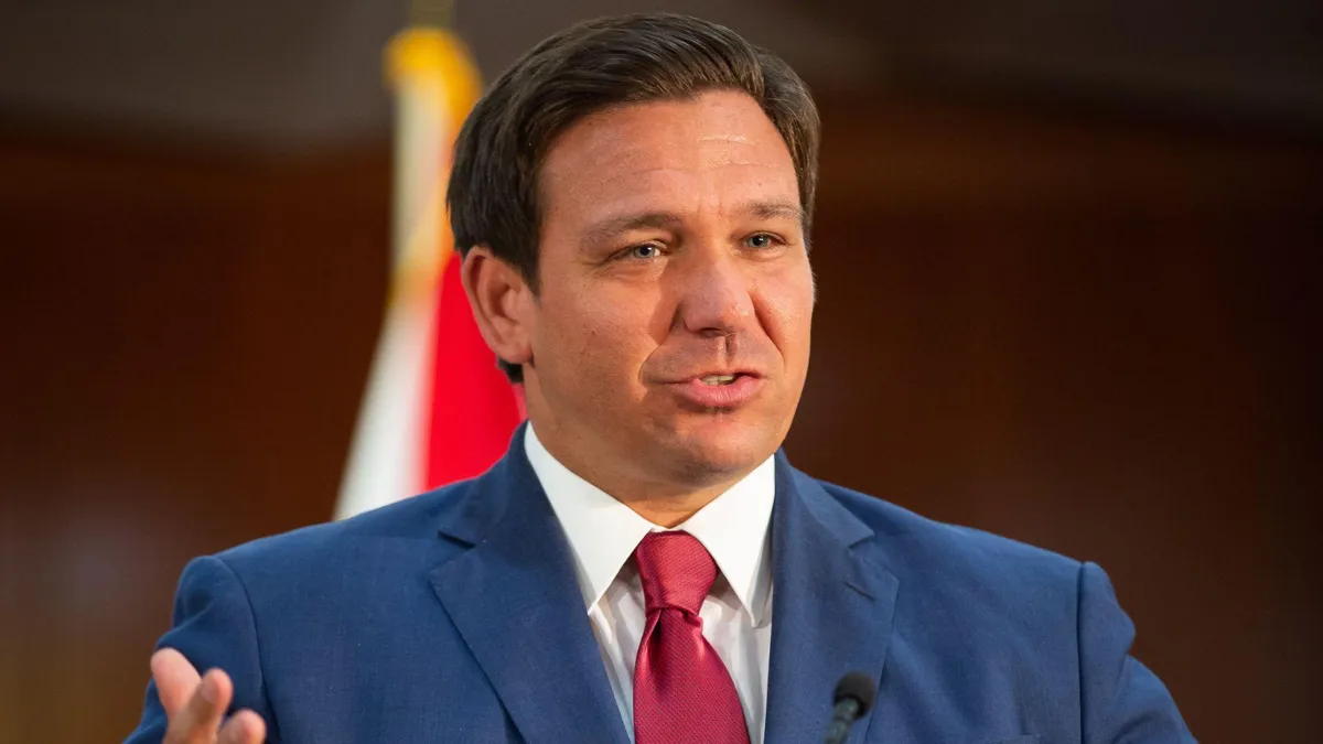 Ron DeSantis wearing a blue suit and red tie while speaking
